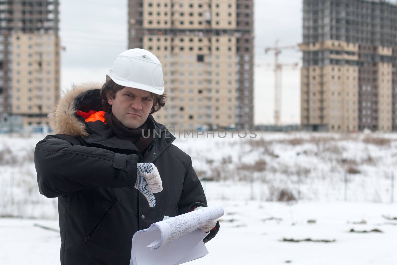 Worker or engineer holding drawing in hands and reading it on background of new apartment buildings and construction cranes on background. Architect engineer concept. Soft focus. by MSharova