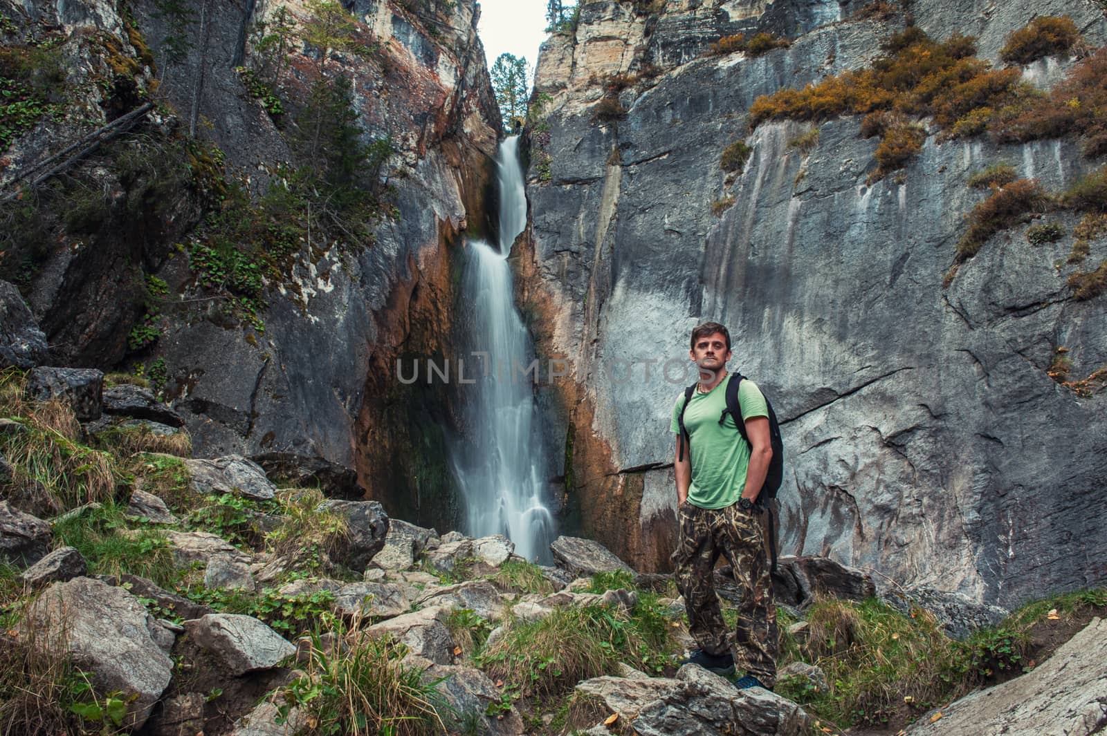 Man with backpack standing in front of waterfall