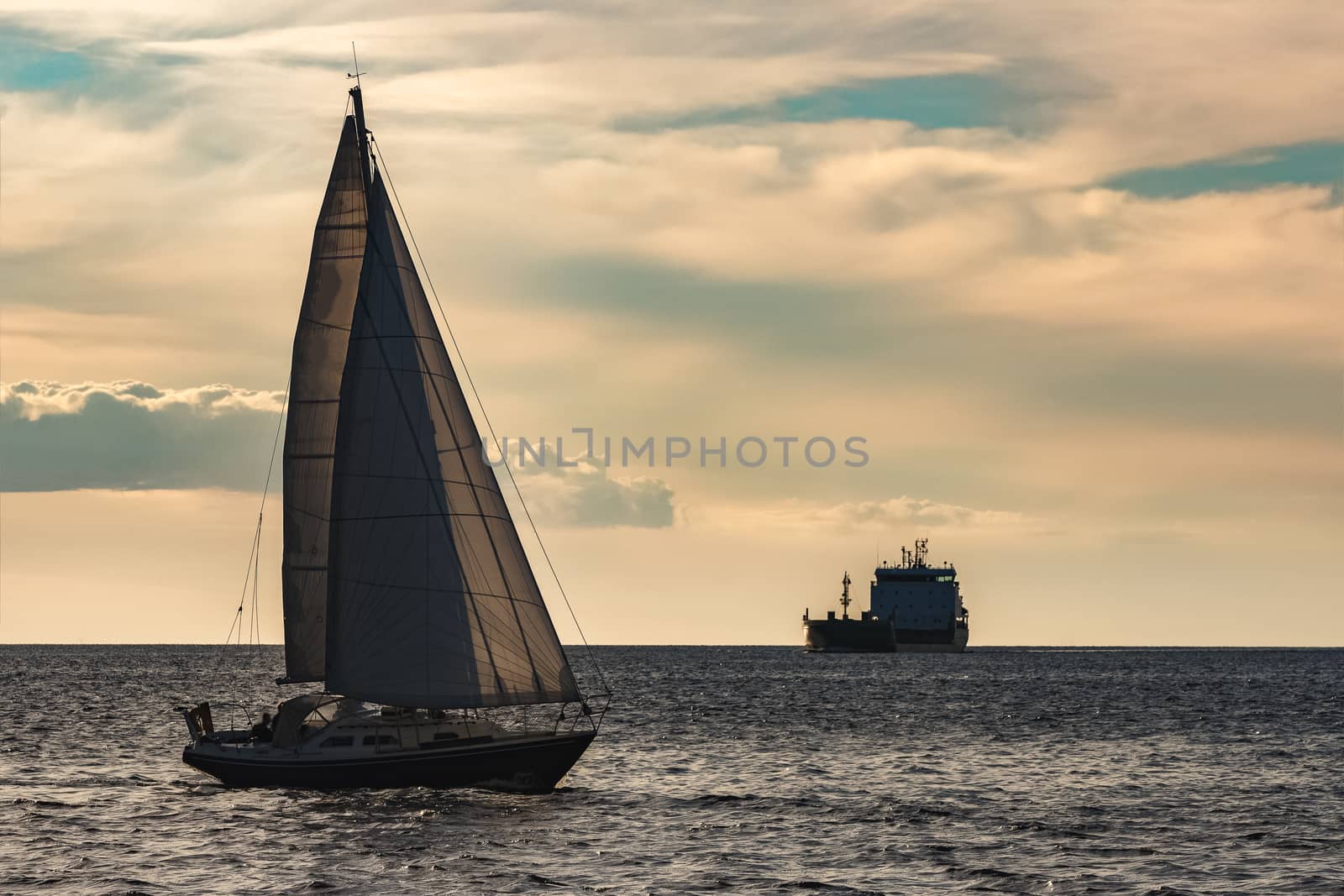 Blue sailboat traveling against the cargo ship in Riga