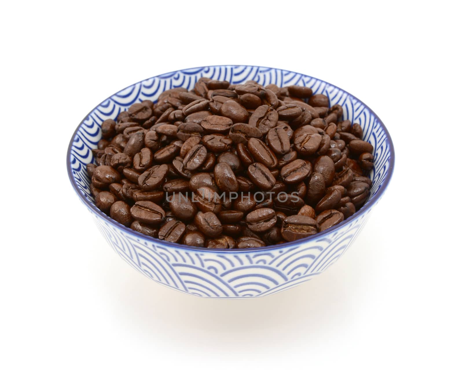 Roasted coffee beans in a blue and white ceramic bowl, on a white background
