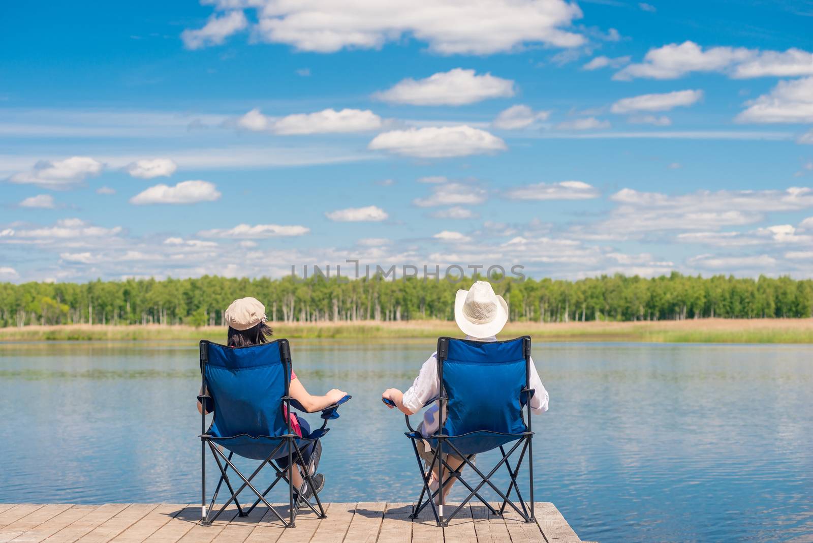 a married couple sitting on chairs near a picturesque lake on a by kosmsos111