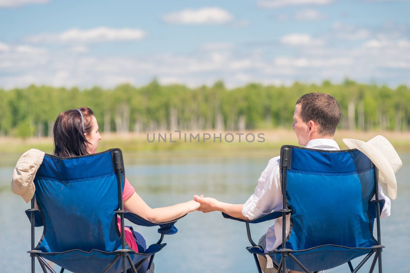 man and woman are sitting on chairs at the pier near the lake and holding hands