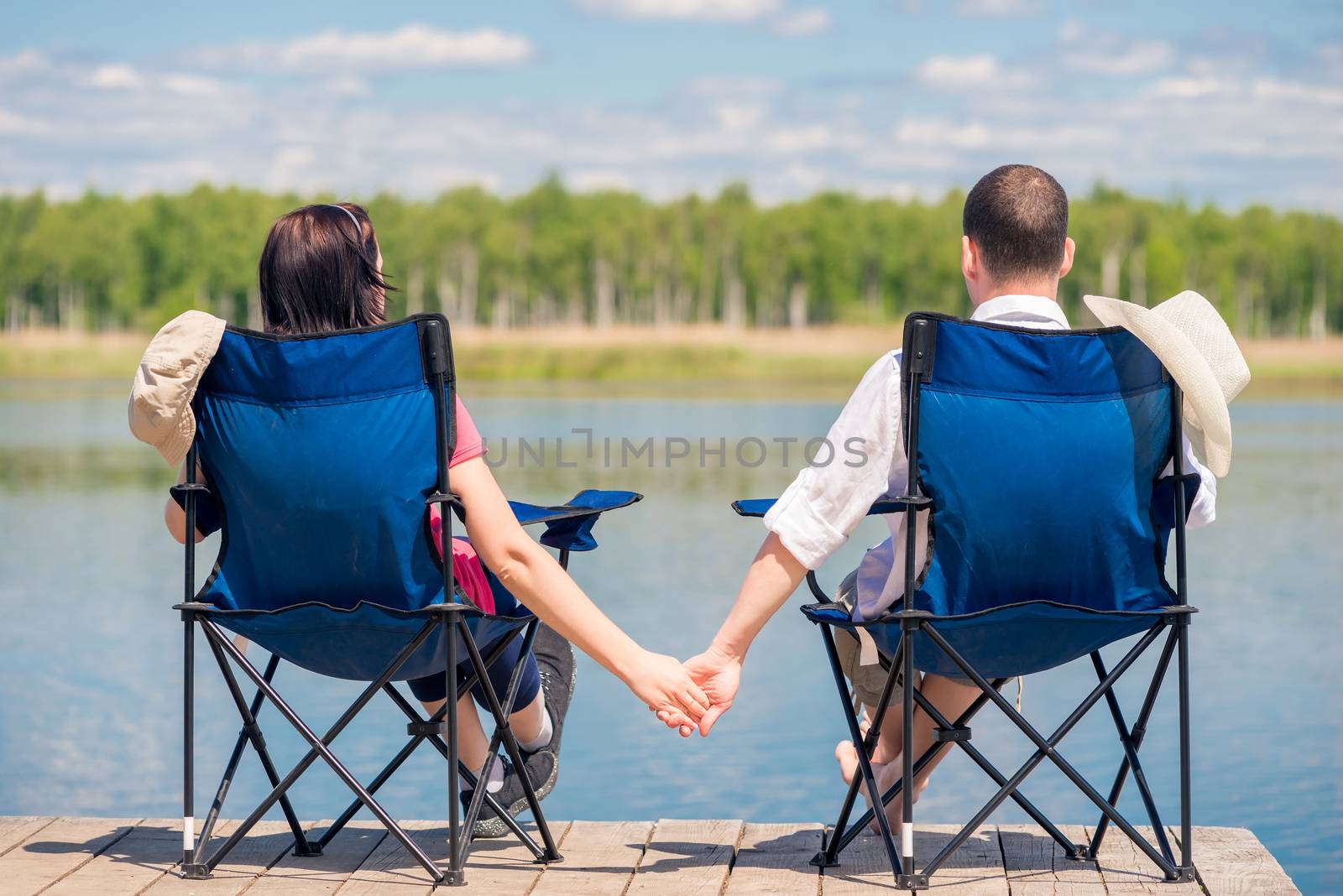 couple sitting on chairs at the pier near the lake and holding h by kosmsos111