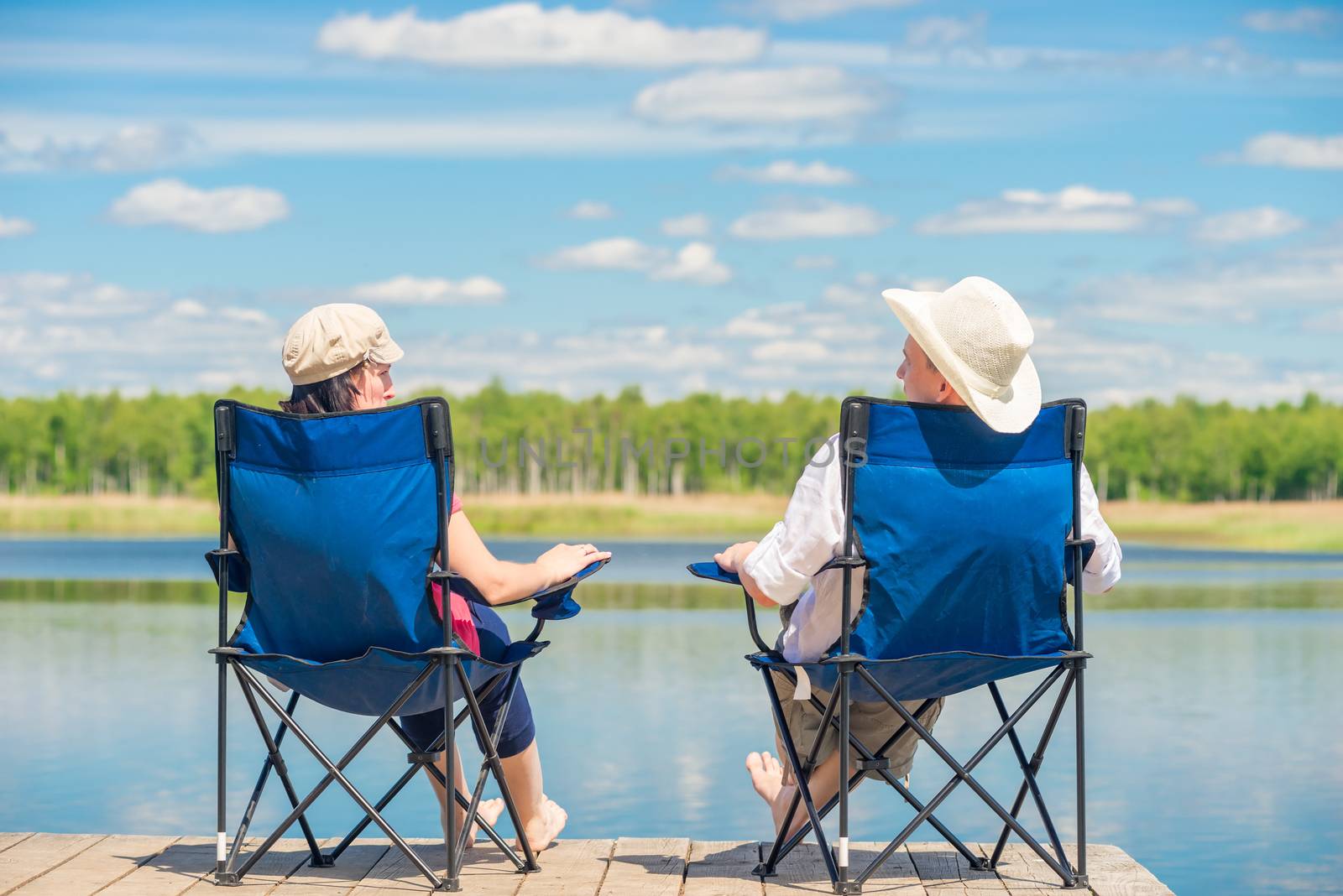 view from the back of a couple on chairs relaxes near a lake on by kosmsos111