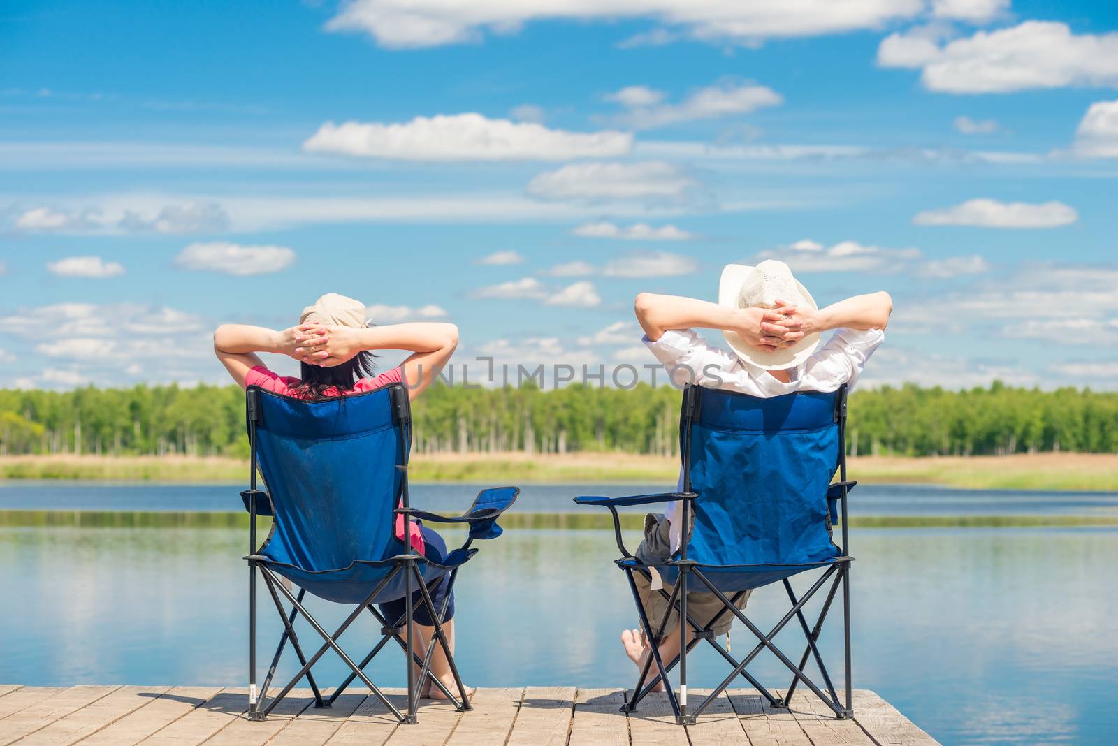 man and woman relax on a pier near a lake sitting on chairs by kosmsos111