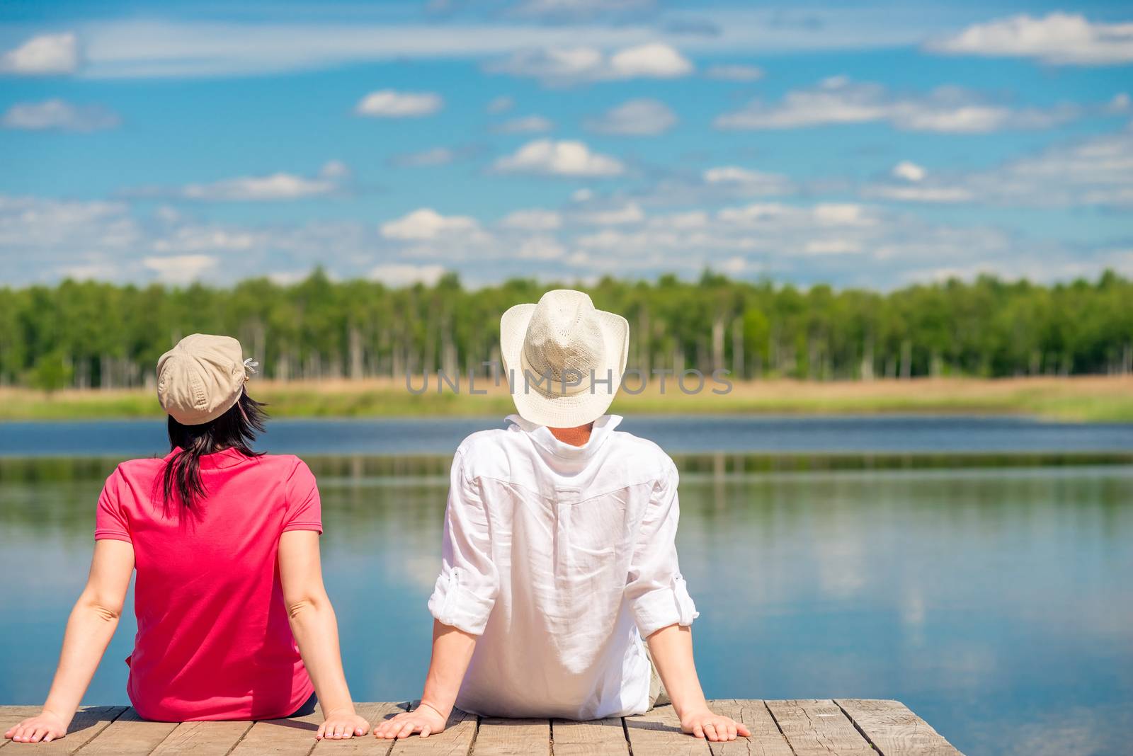 a loving couple enjoying a beautiful lake sitting on a wooden pi by kosmsos111