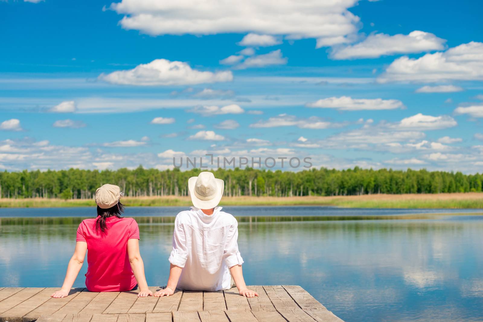 young couple enjoying a beautiful lake sitting on a wooden pier by kosmsos111