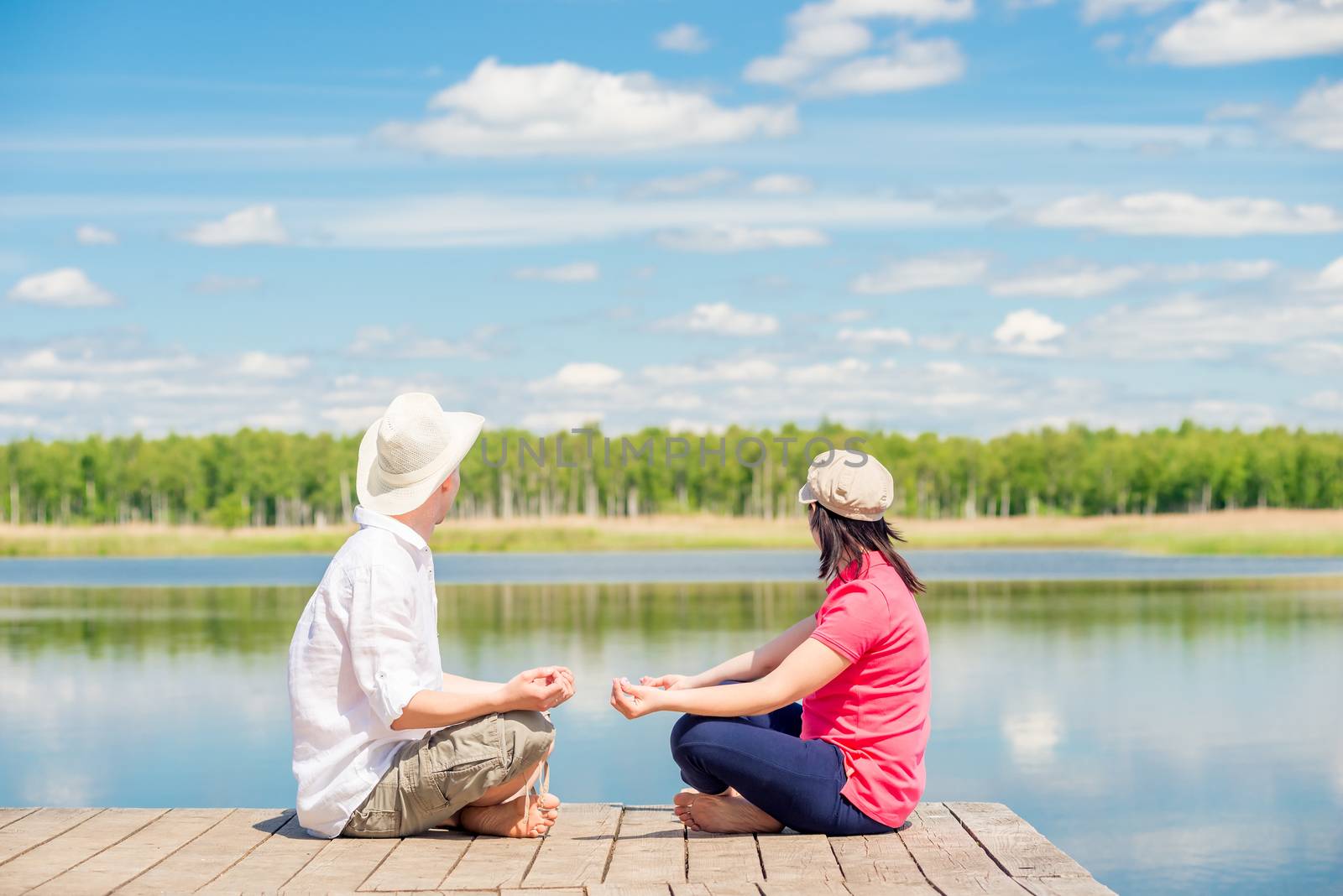 couple in love relax in a lotus pose on a wooden pier near the lake