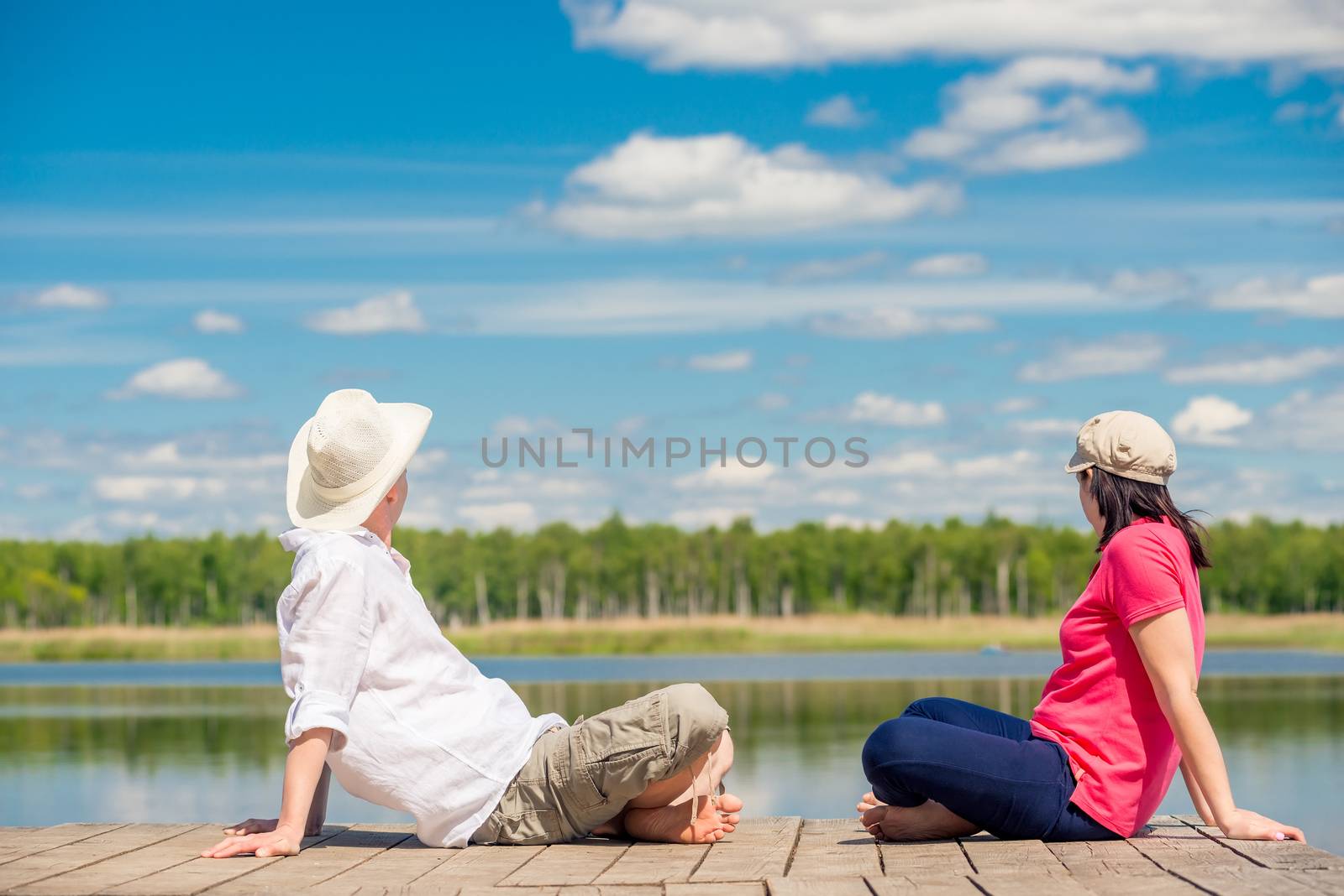 man and woman on a wooden pier sit and admire the beautiful lake