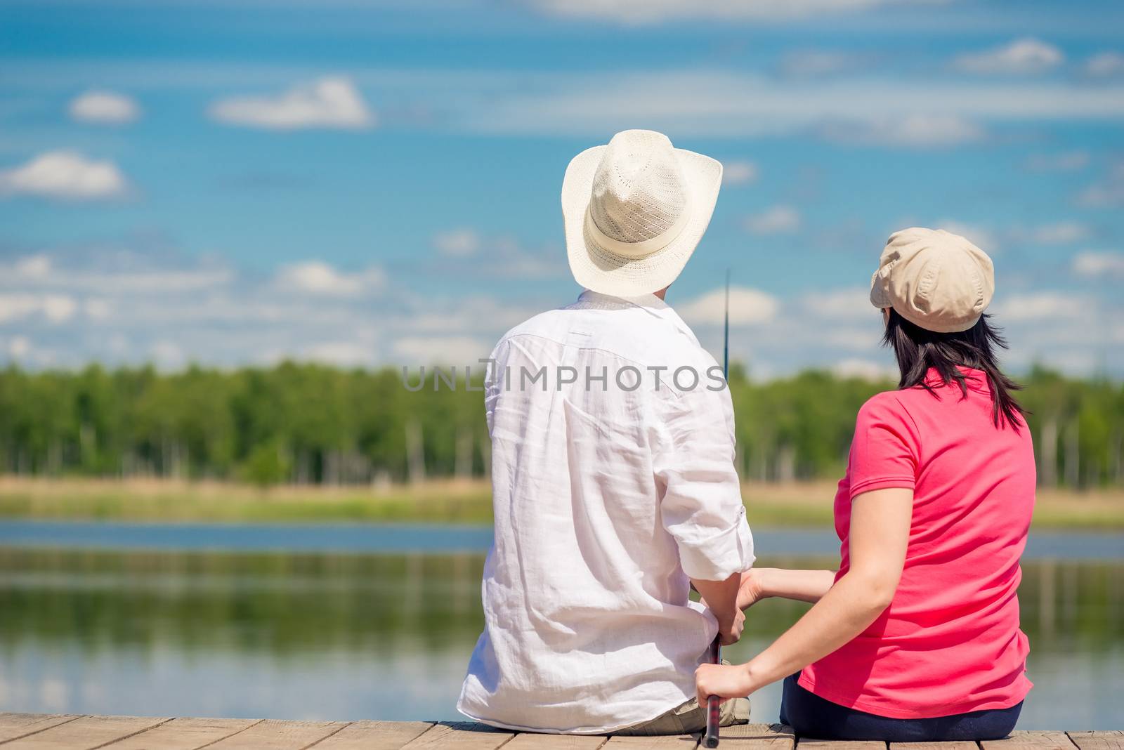 family couple with a fishing rod sitting on a wooden pier near the lake, rear view