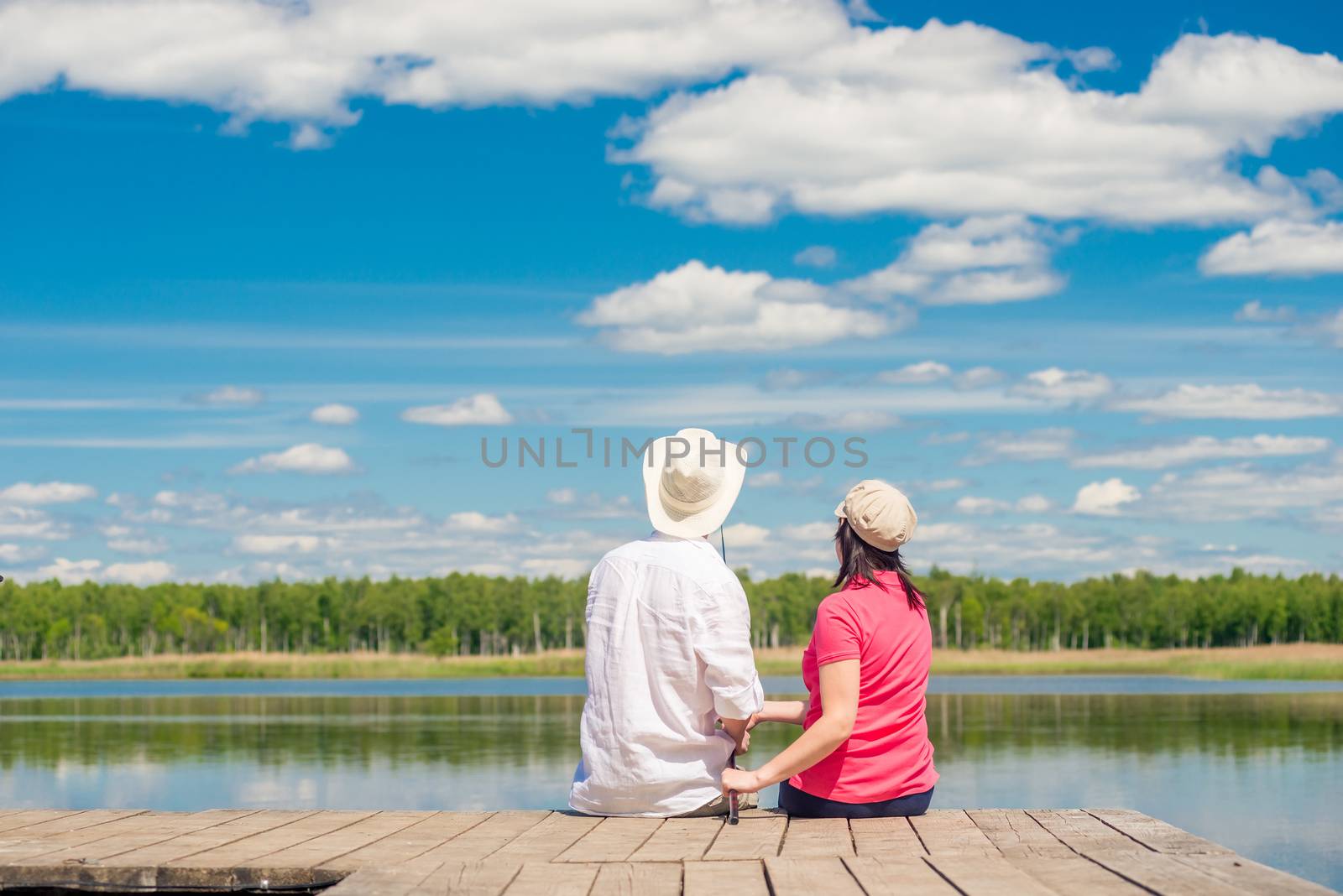 young couple with a fishing rod sitting on a wooden pier near th by kosmsos111