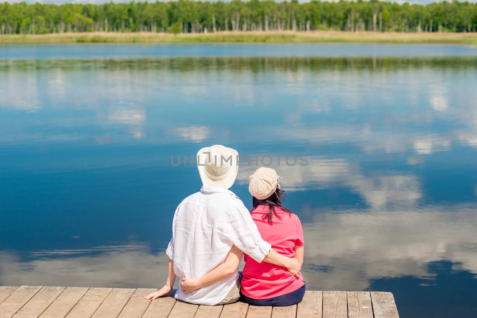 young happy couple hugging and enjoying rest near beautiful lake, view from back