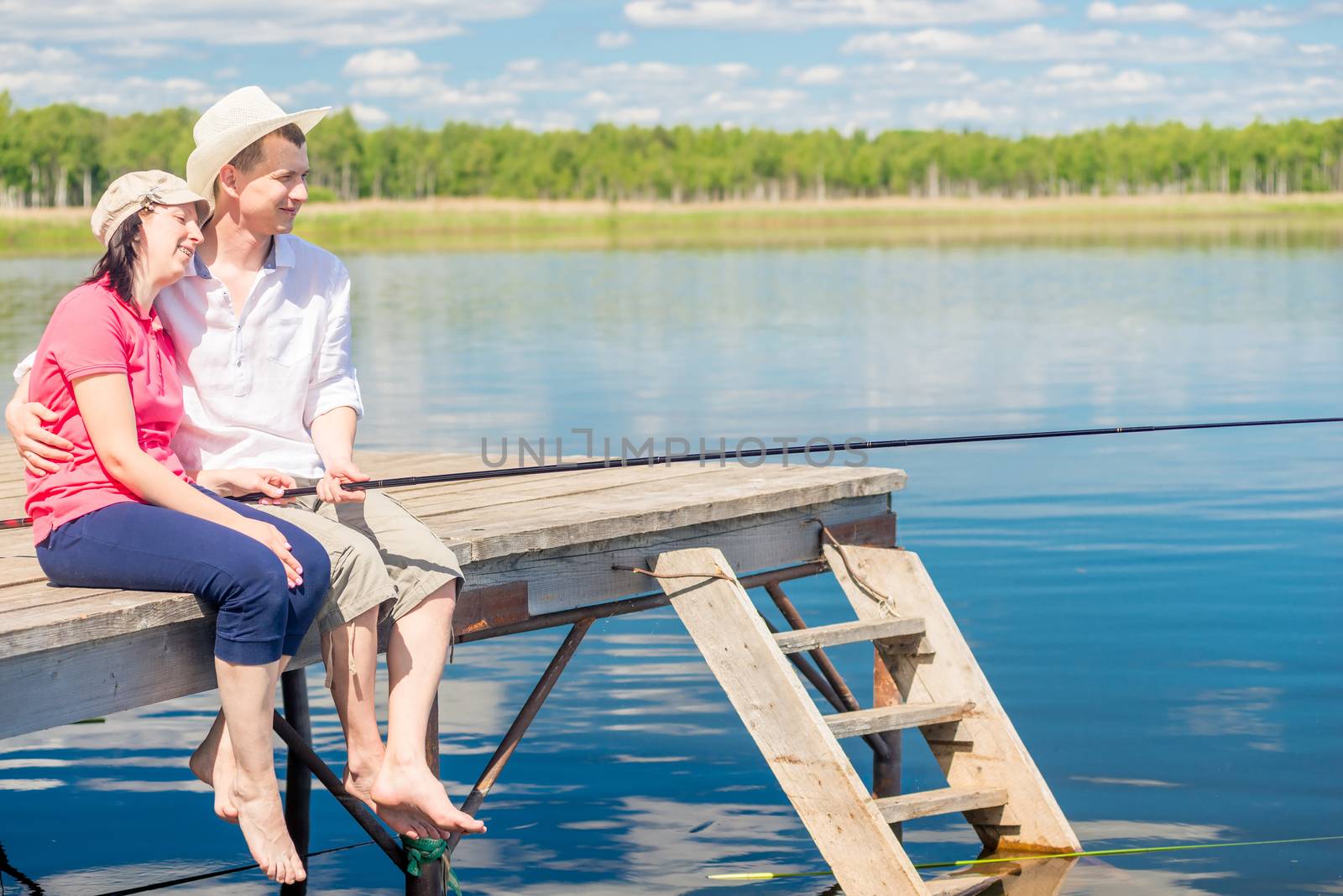 A married couple on a pier with bare feet catching a fish on a beautiful lake