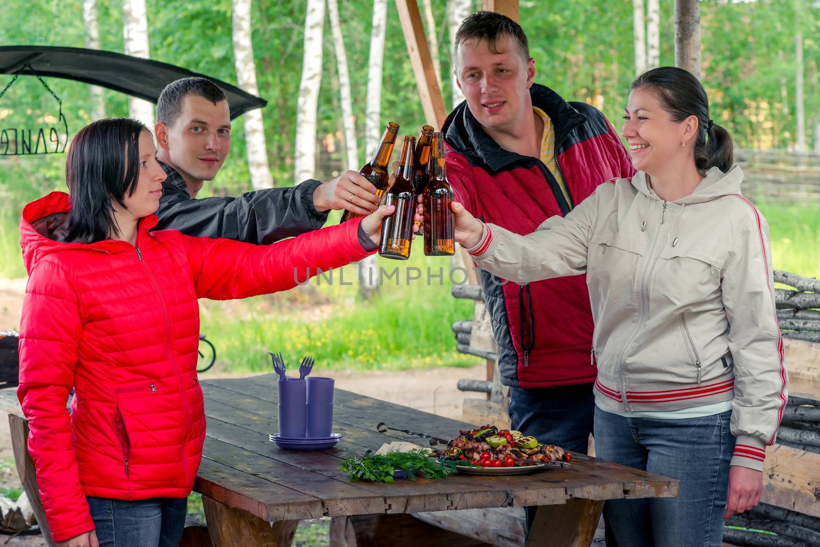 four friends with a shish kebab and beer in the nature in the gazebo