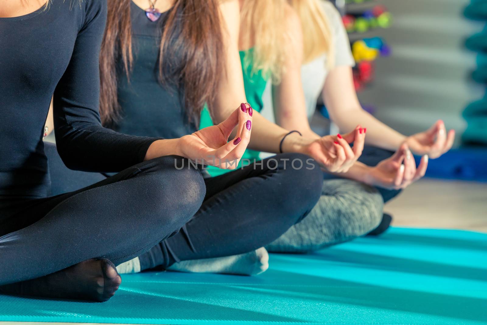 knees and hands of women sitting in a lotus pose in the gym close up