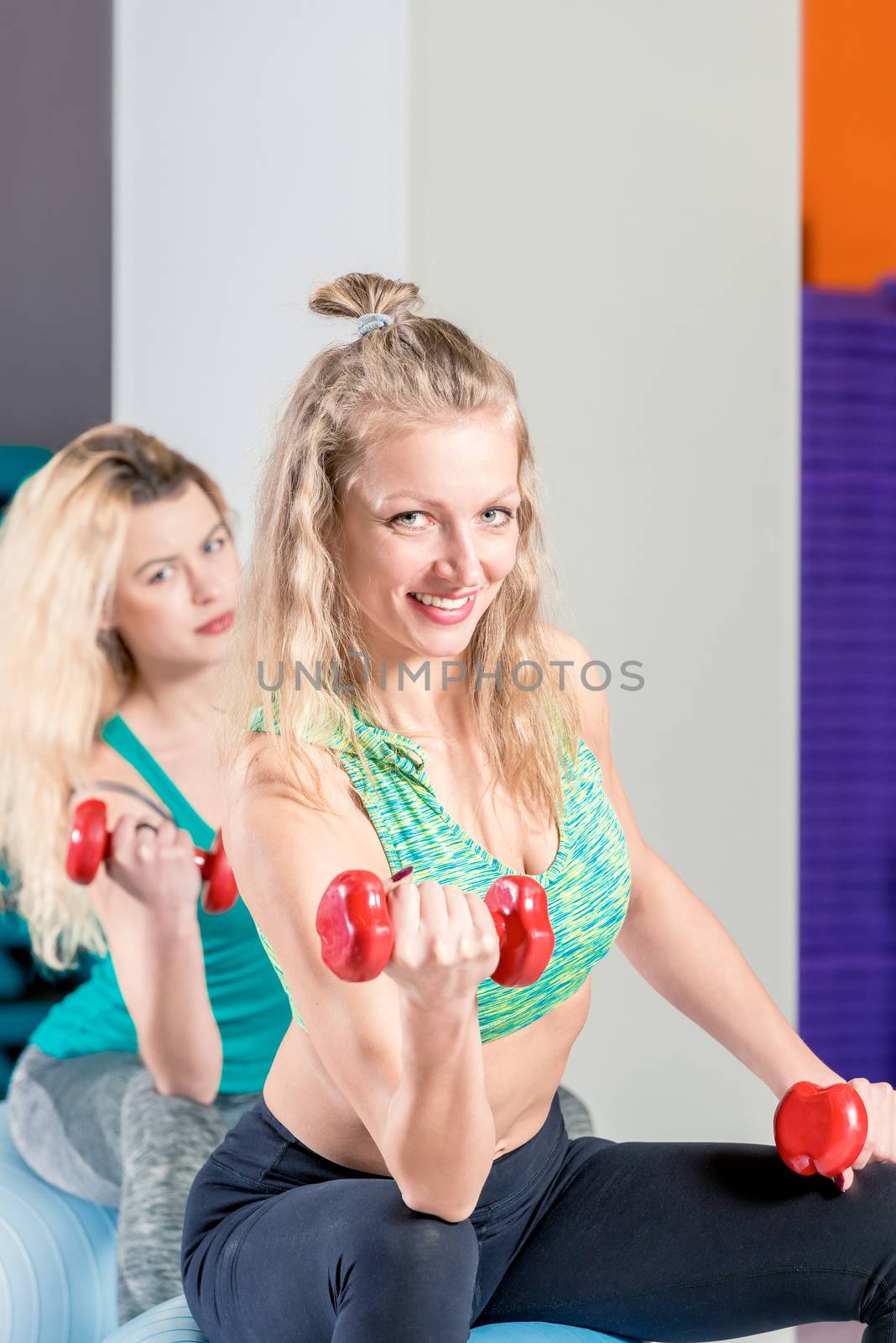 vertical portrait of a cute blonde with red dumbbells during a workout in the gym