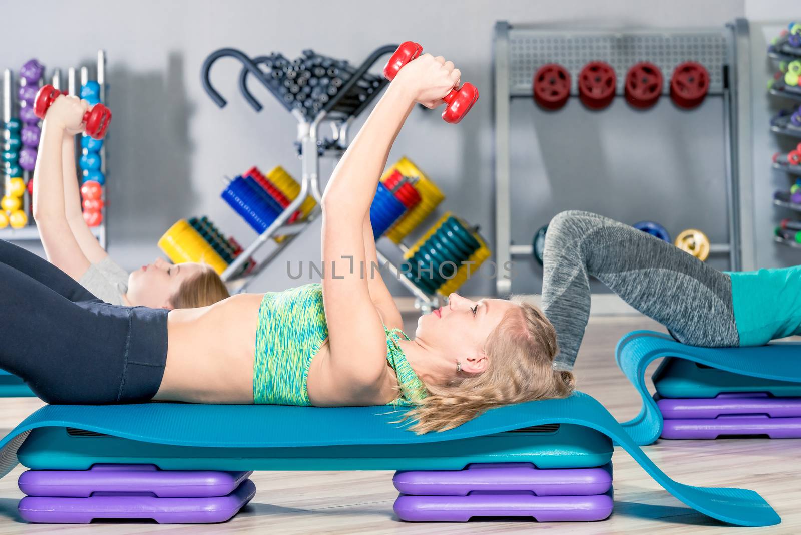 woman lifting dumbbells lying down, class at the gym in a group