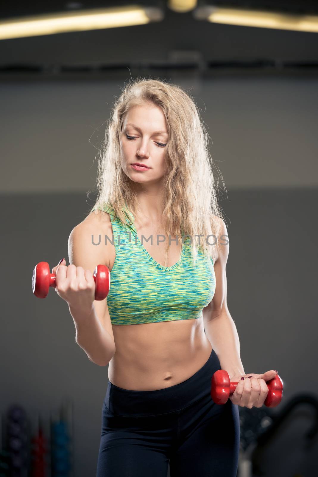 blonde in sportswear with dumbbells on training in the gym