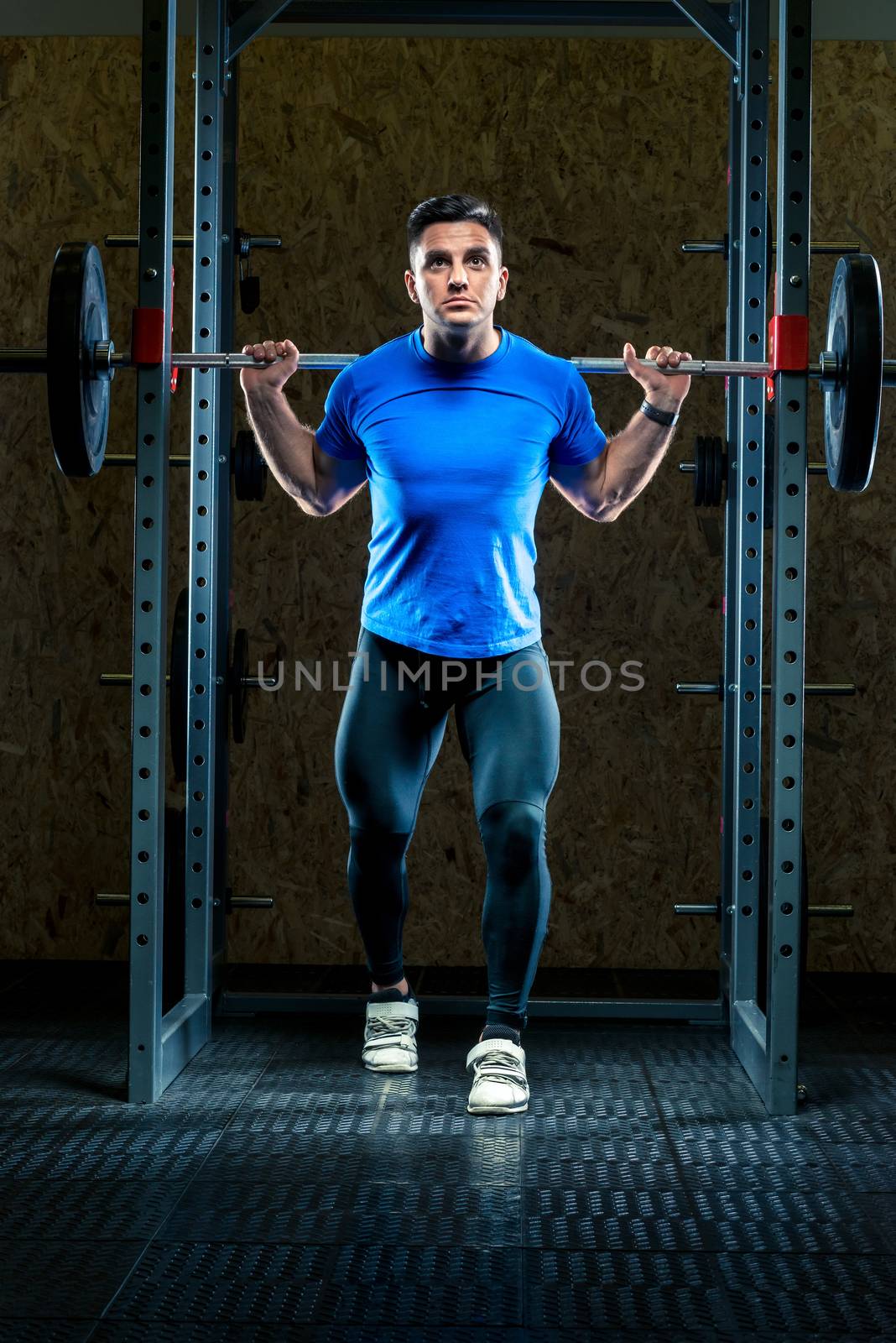 vertical portrait of a strong athlete at a training session in a gym with a barbell