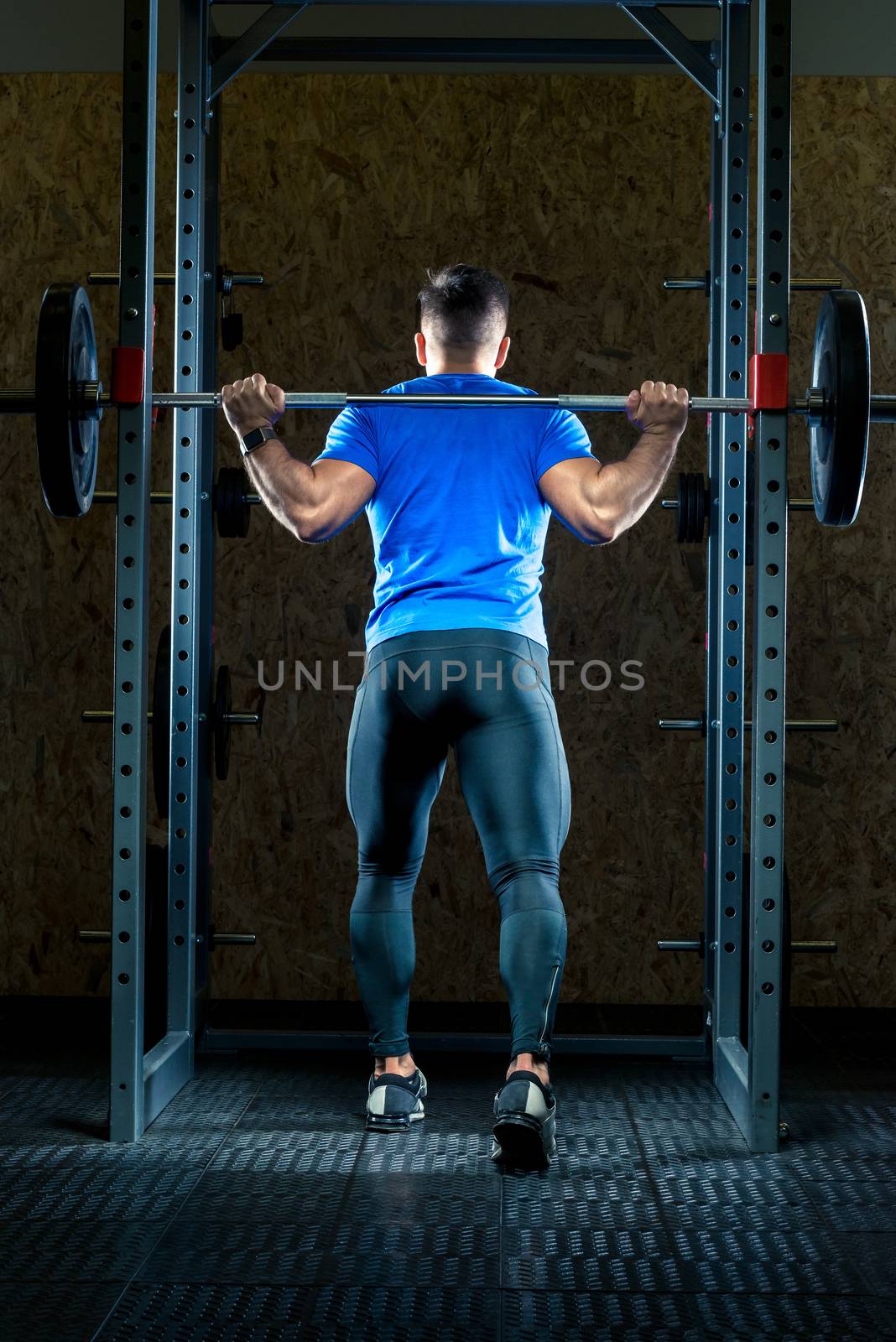 athlete in training in the gym with a barbell, view from the bac by kosmsos111