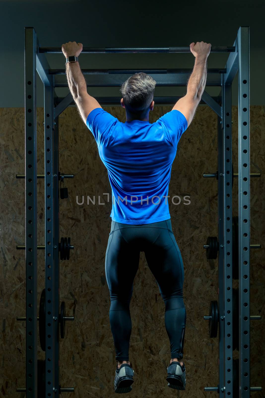 view from the back of an athlete pulls up on the bar in the gym