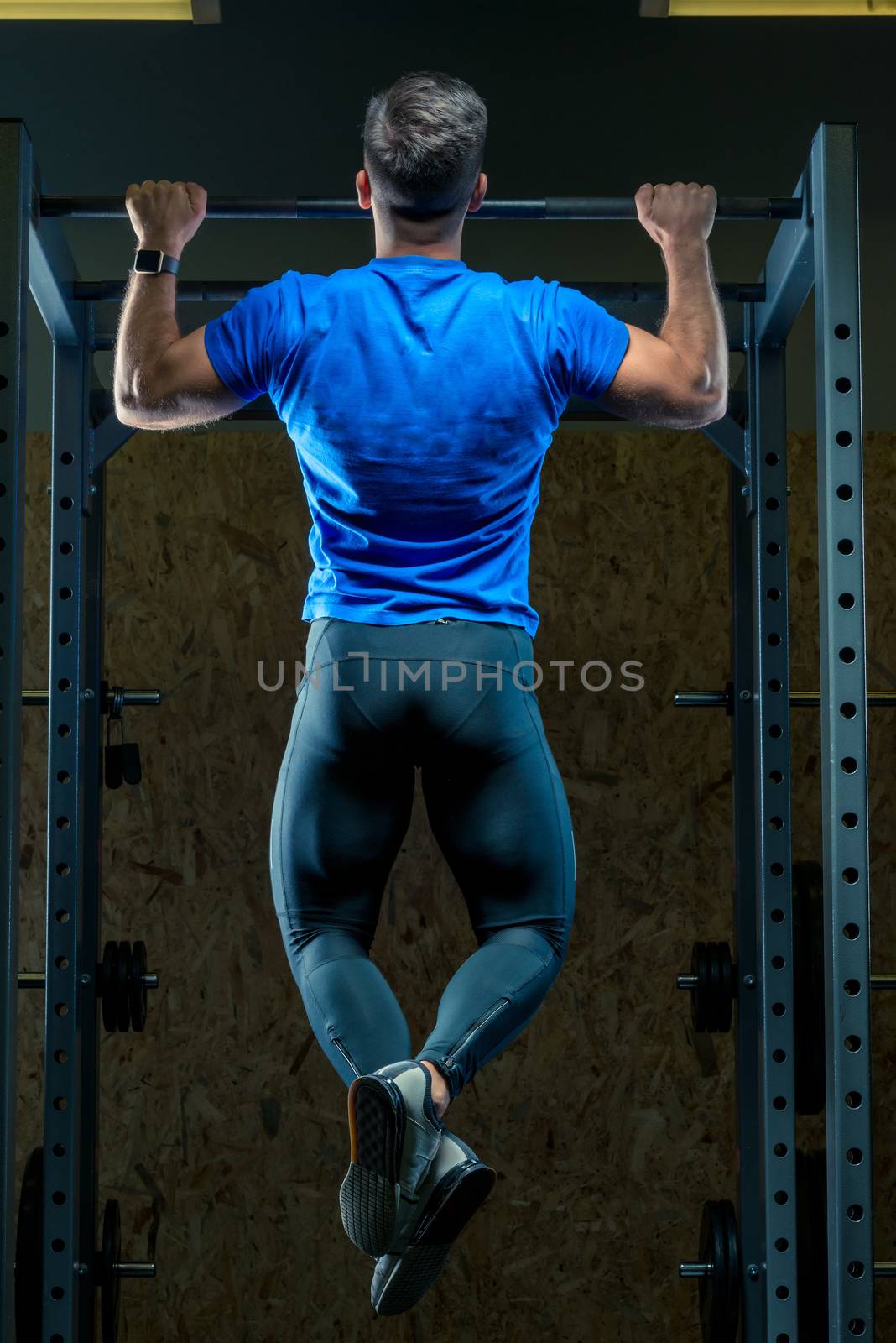 the athlete pulls himself up on the bar in the gym view from the back