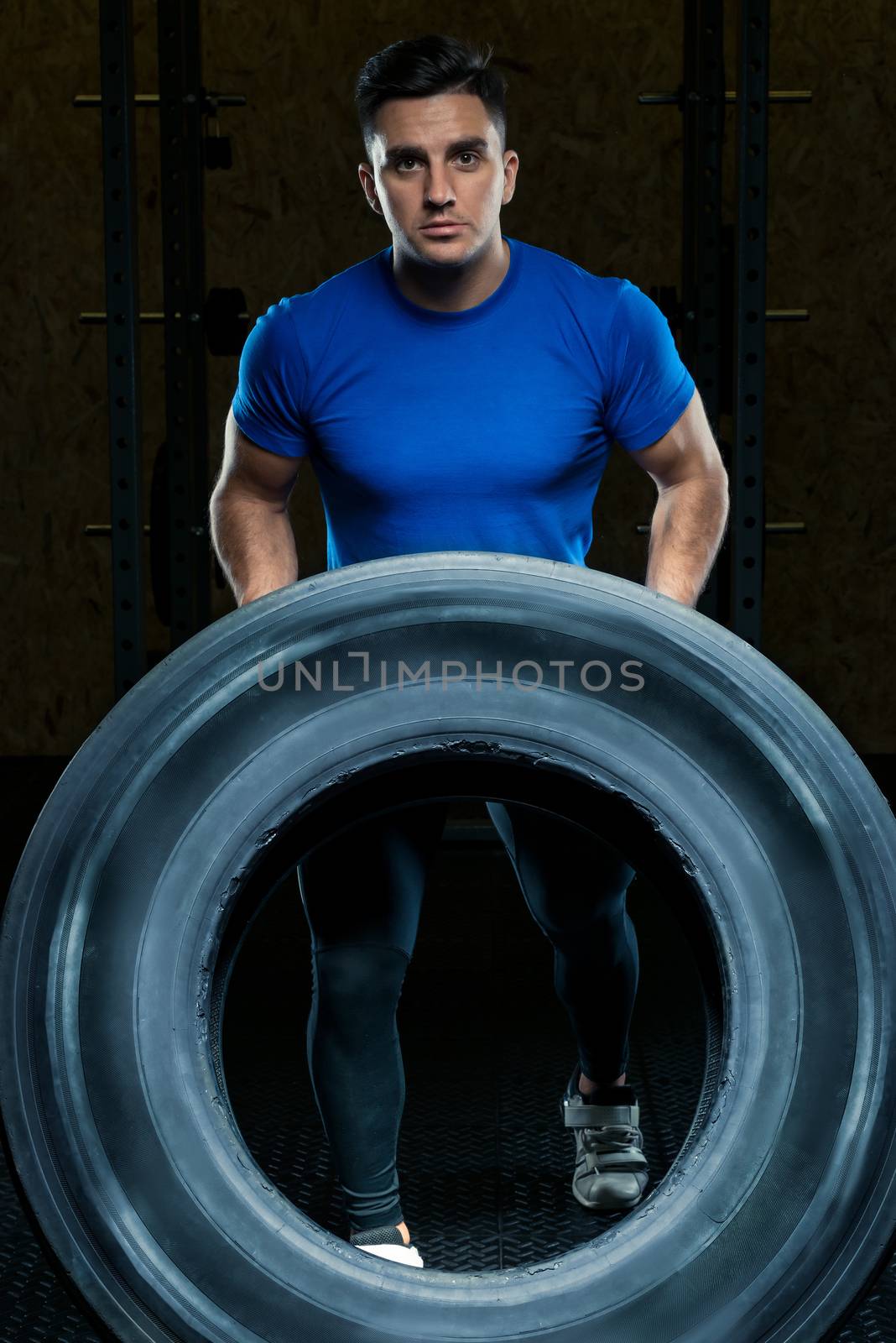portrait of a strong athlete with a large heavy wheel in the gym by kosmsos111