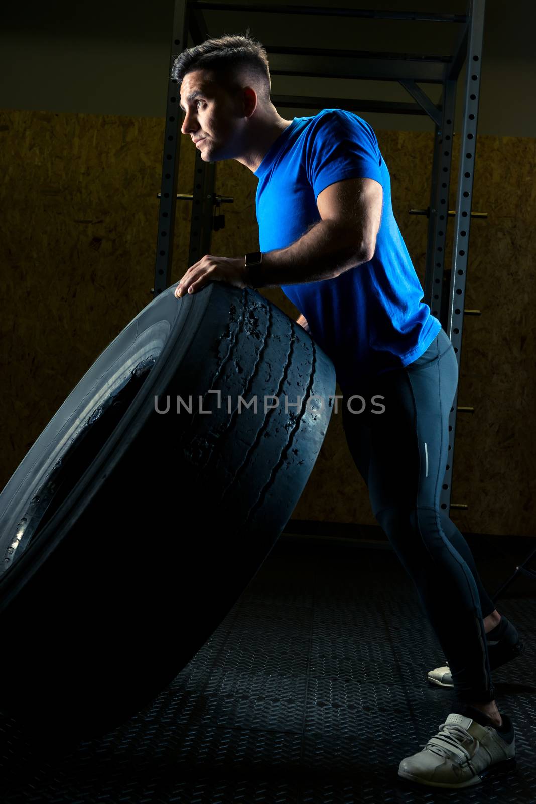 strong young athlete with a large heavy wheel in the gym by kosmsos111