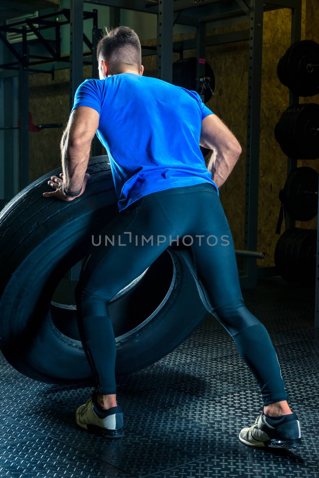 bodybuilder exercises in the gym with a heavy wheel, the view from the back
