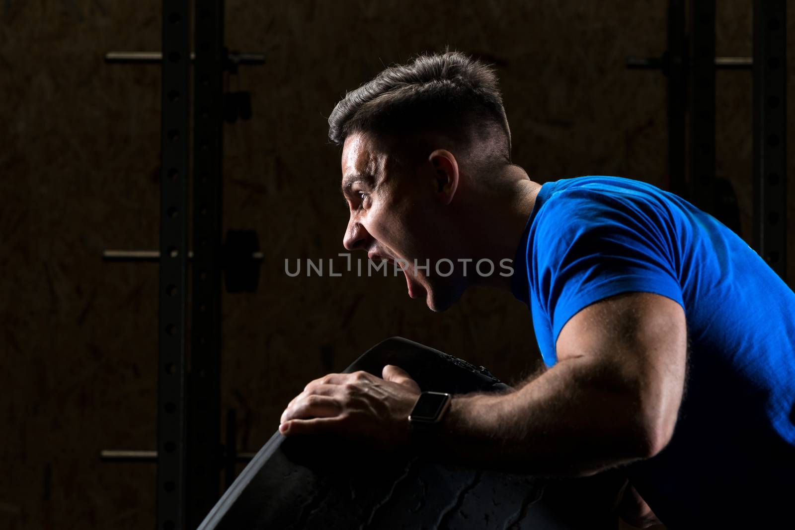 screaming sportsman bodybuilder lifts a heavy heavy wheel, close-up portrait