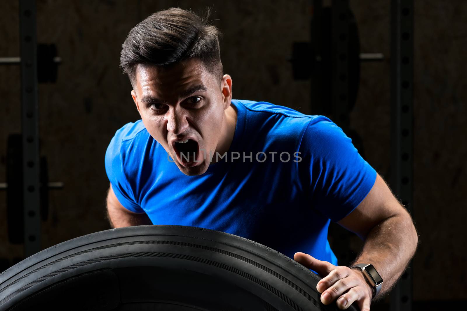 close-up portrait of a screaming sportsman bodybuilder lifting a heavy large wheel