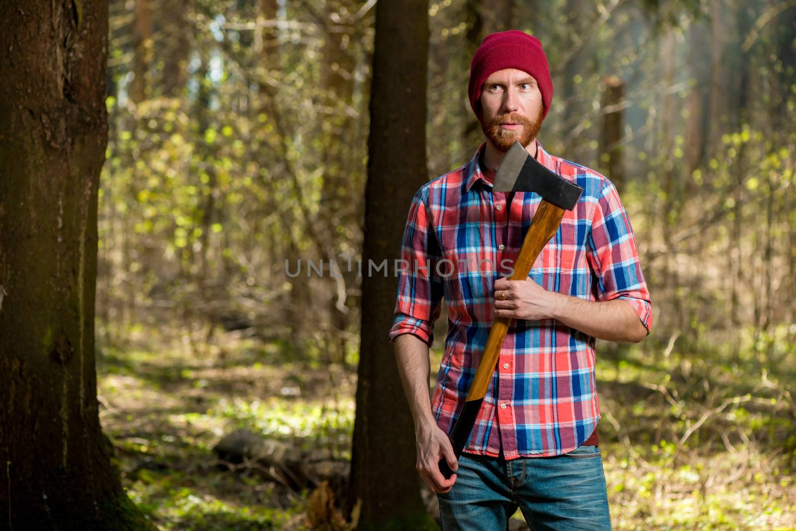 portrait of a bearded hipper forest ranger in a forest with an ax