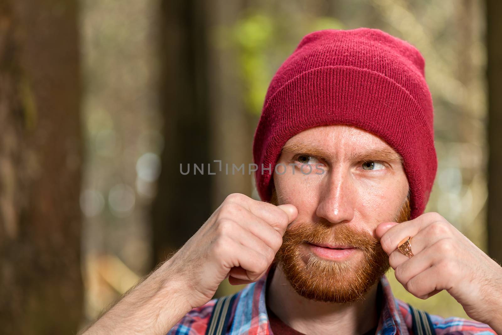 horizontal portrait of a man in a hat who adjusts his mustache close-up