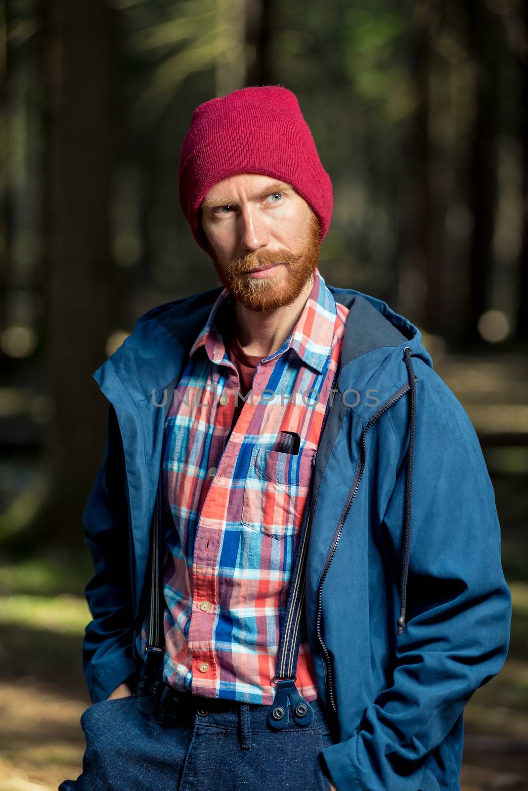 stylish man with beard in hat and jacket posing in forest