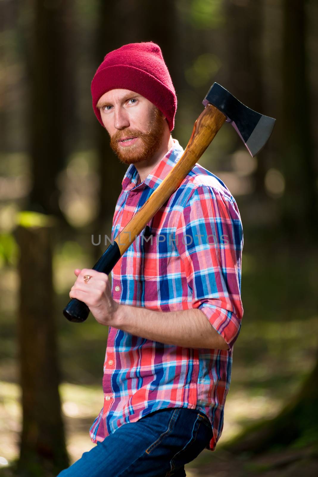 portrait of a serious hipster forester with an ax in the woods by kosmsos111