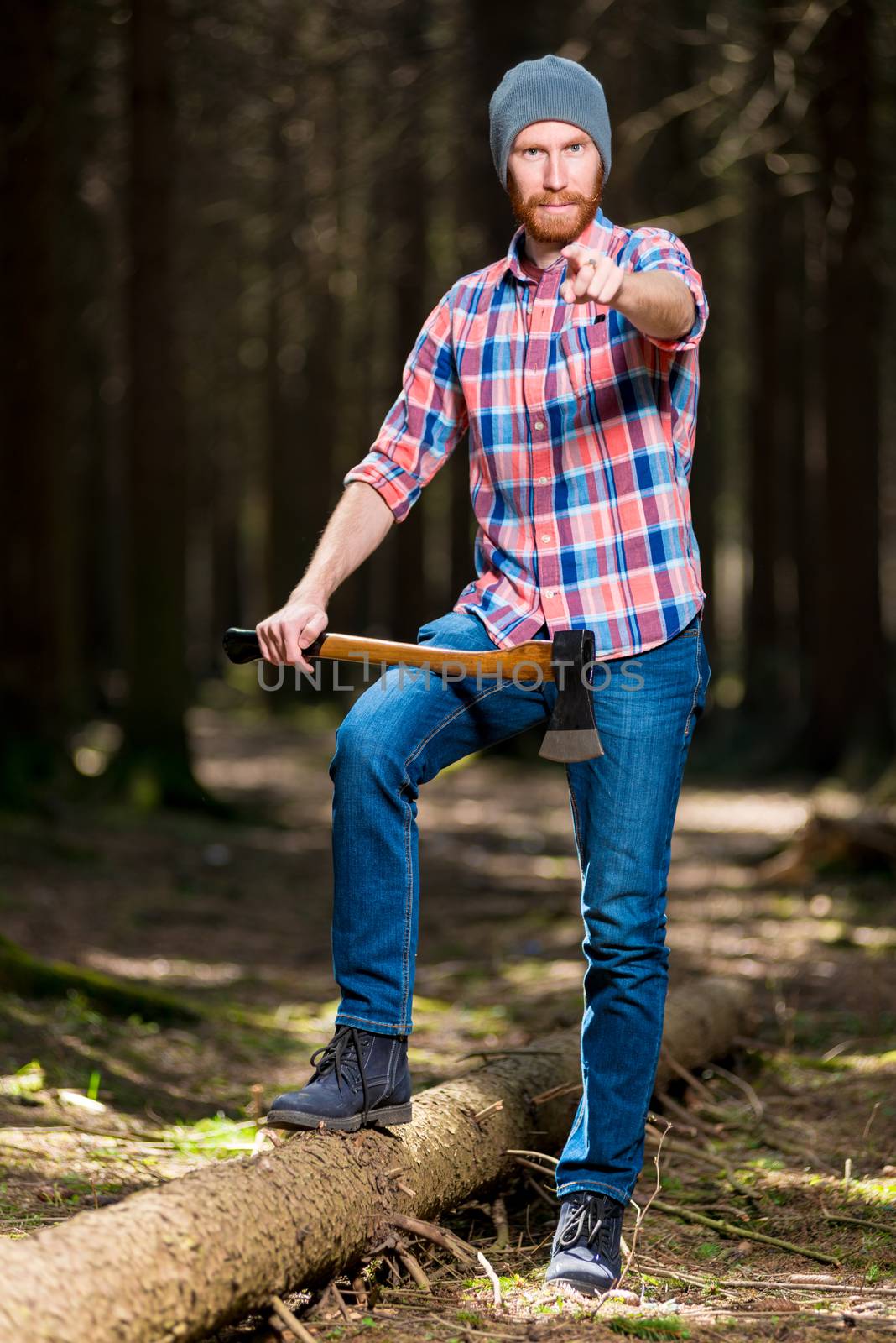 a bearded forester with an ax points to the camera with his finger in the woods