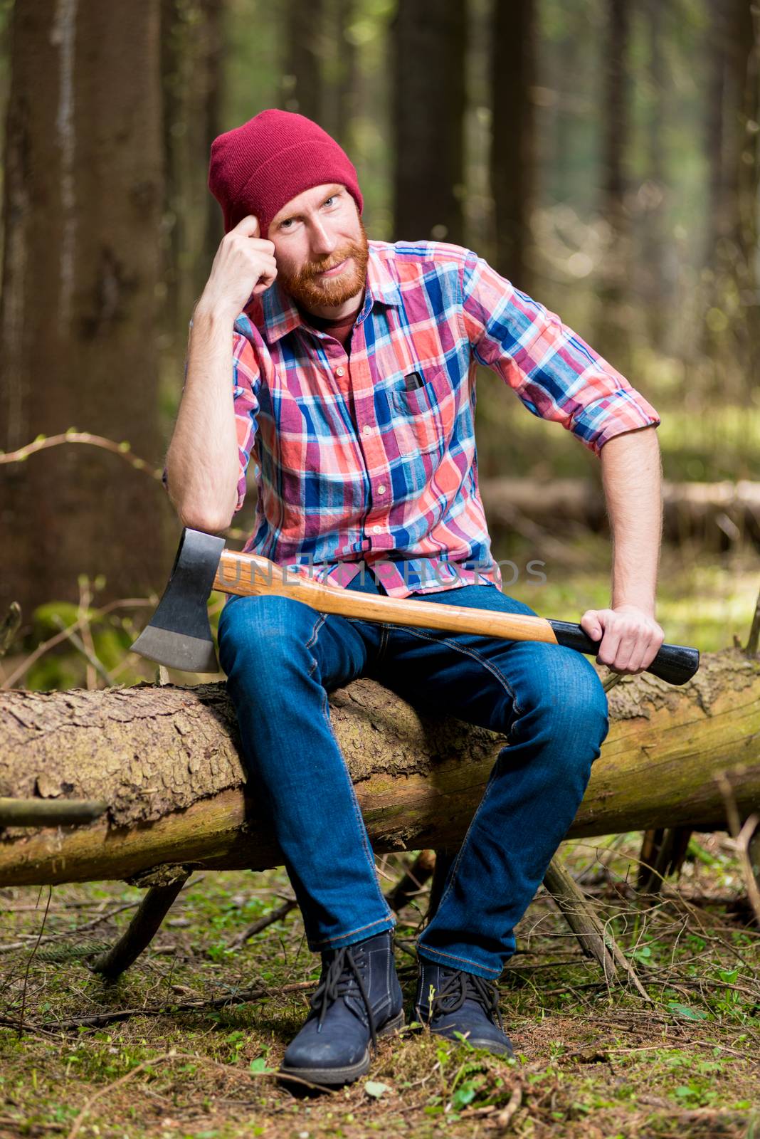 thoughtful lumberjack in a hat and shirt with an ax sits on a log in the woods