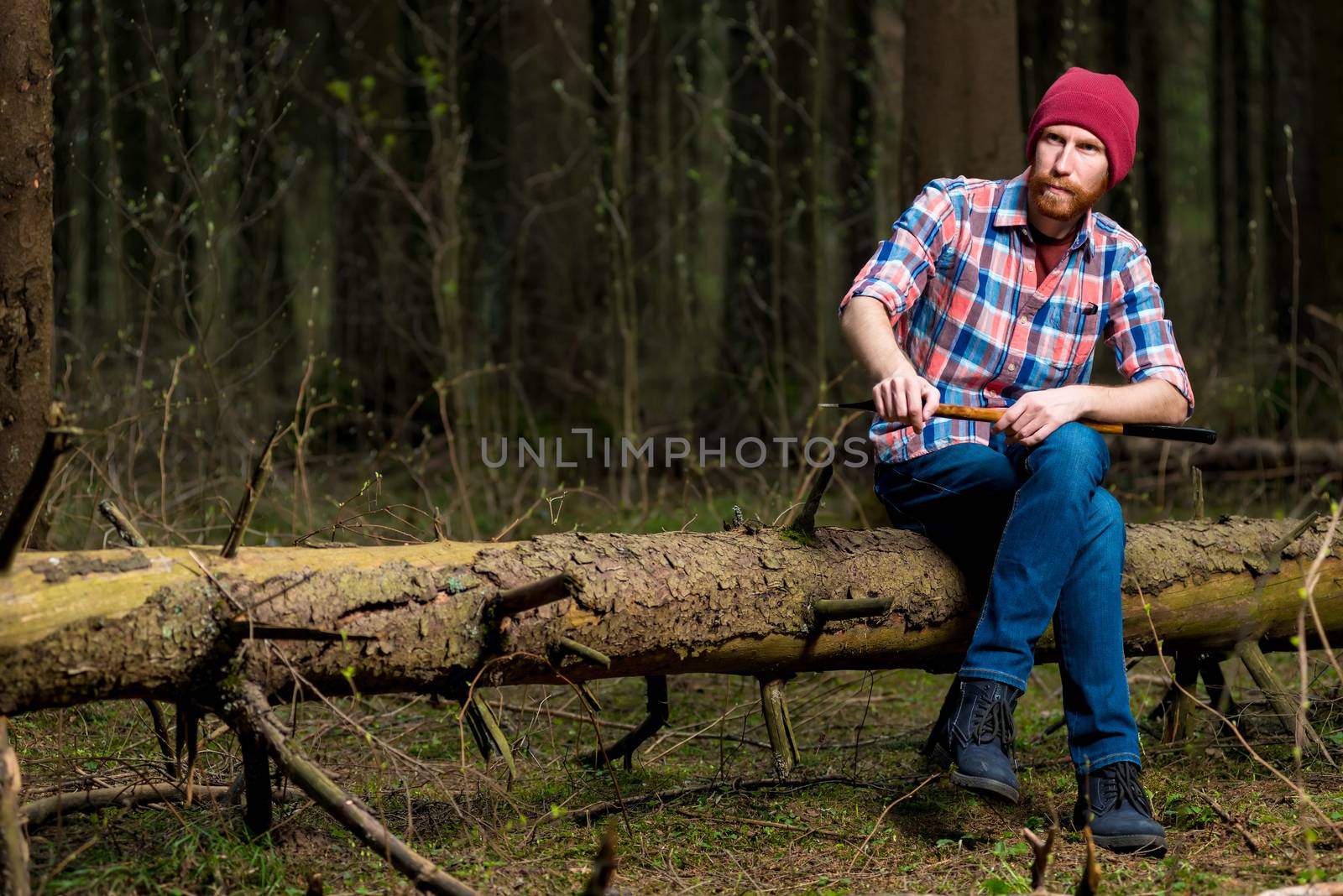 portrait of a forester in a plaid shirt with an ax sitting on a log