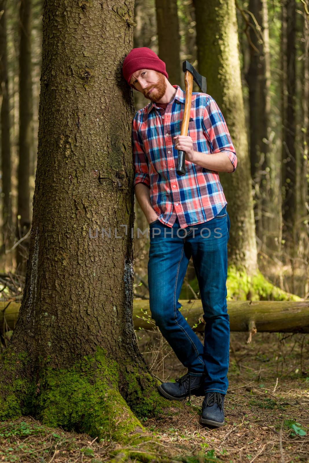 tired bearded lumberjack with an ax resting, leaning against a tree