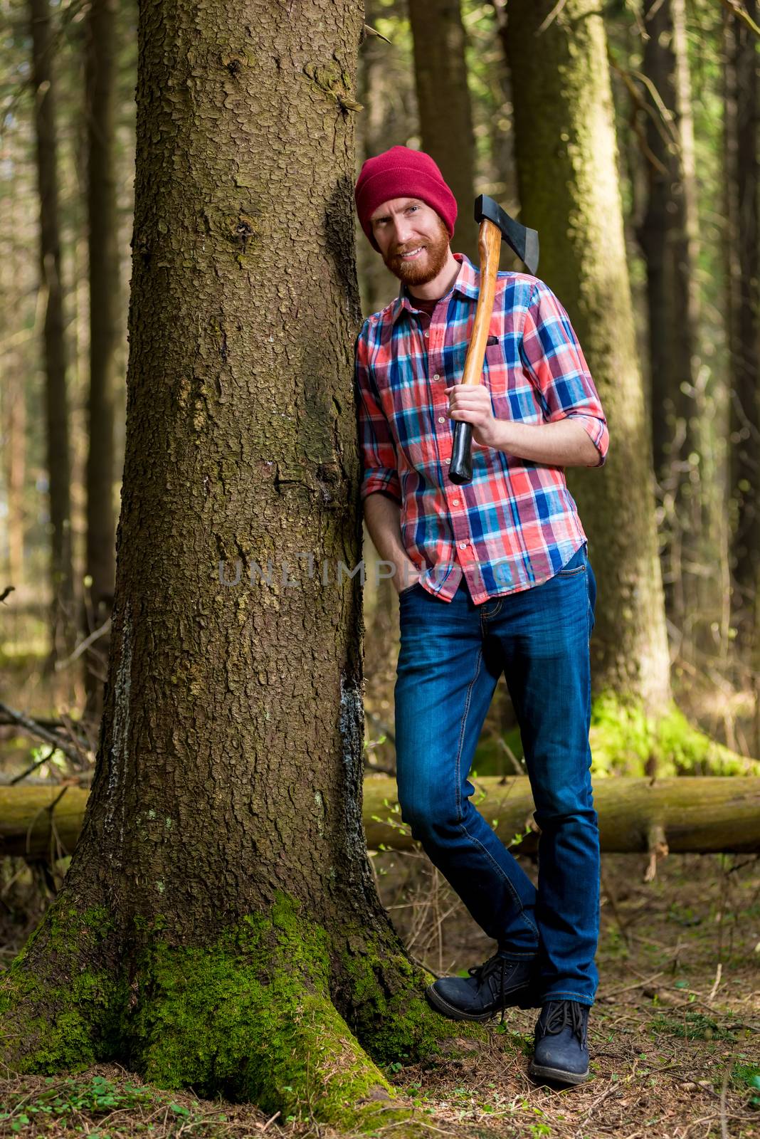 a smiling forester with an ax resting, leaning against a tree