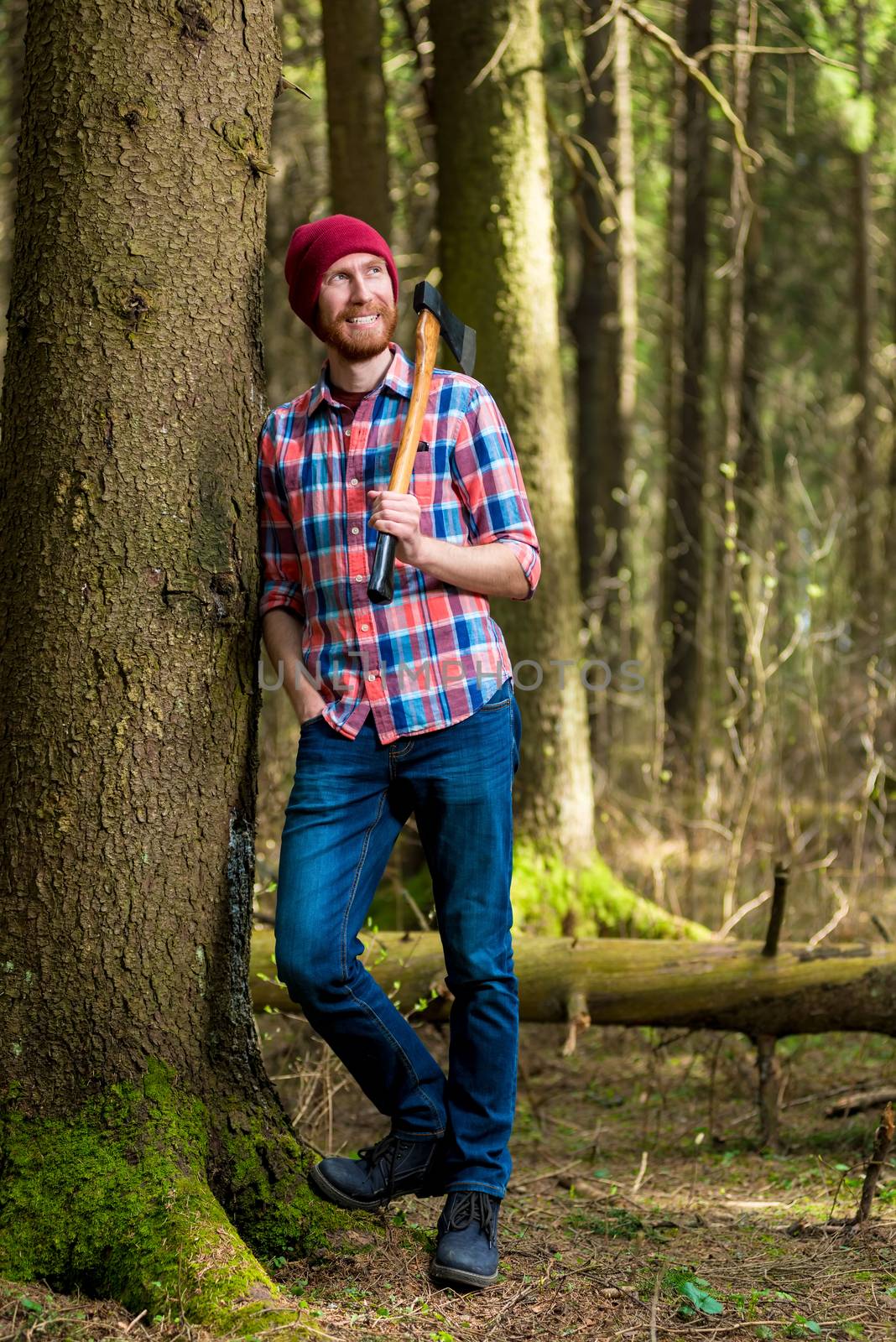 dreamy forester resting with an ax, leaning against a tree