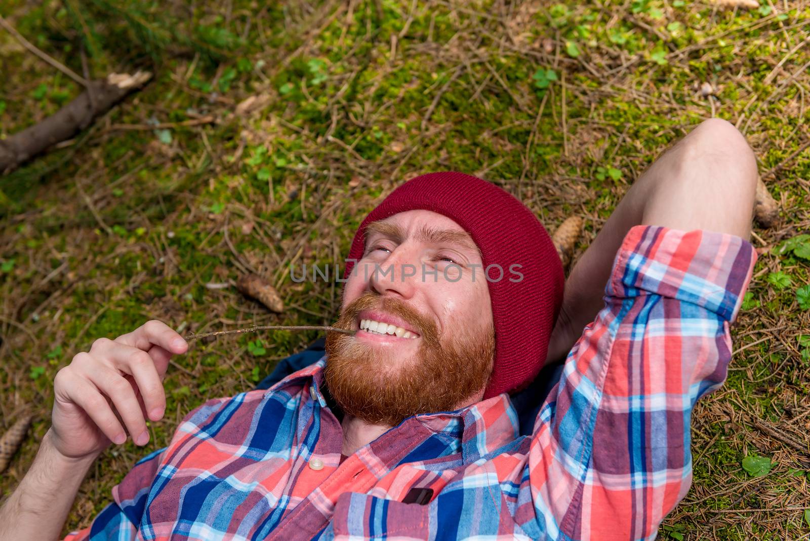 close-up portrait of a happy man with a beard lying on the ground in the forest