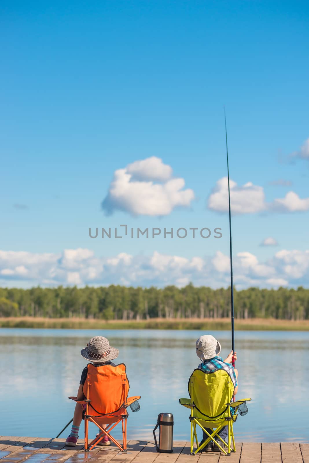 A boy and a girl on a wooden pier are fishing in a clean lake by kosmsos111