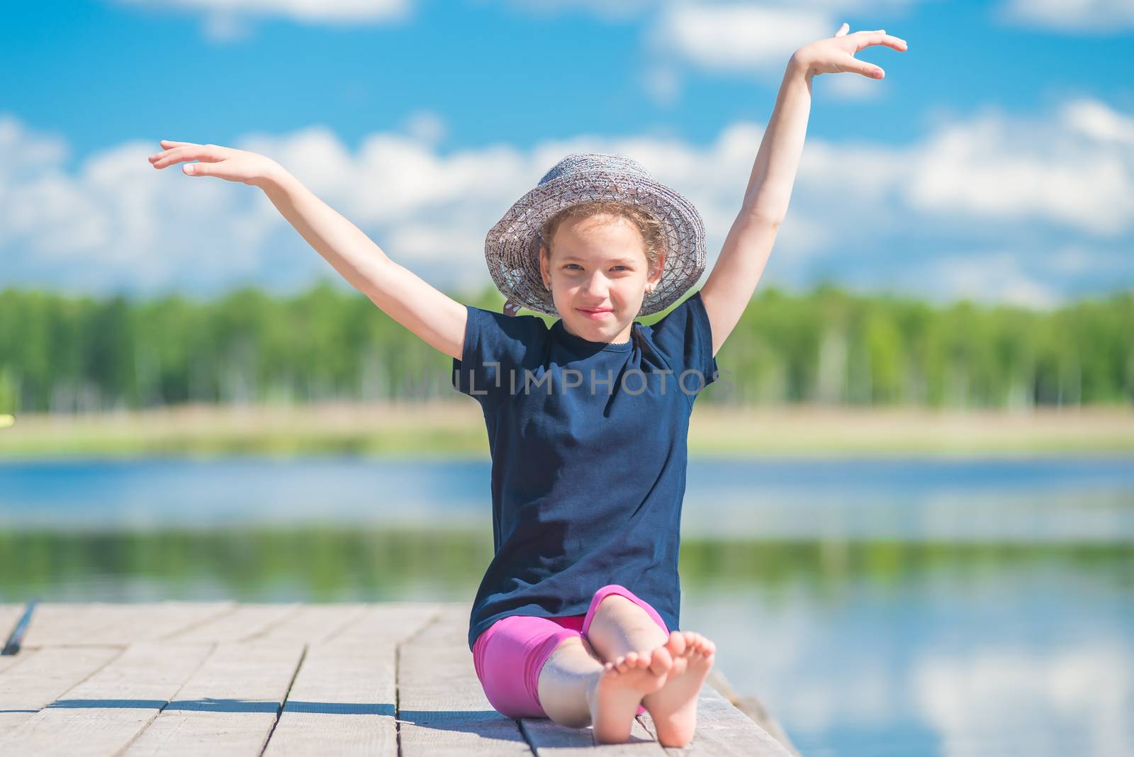 girl in a hat sits on a wooden pier near a lake and poses by kosmsos111