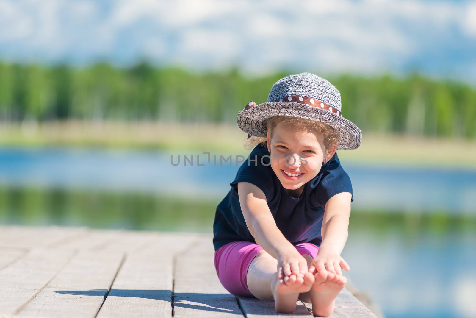 happy girl in a hat sits on a wooden pier near the lake and poses