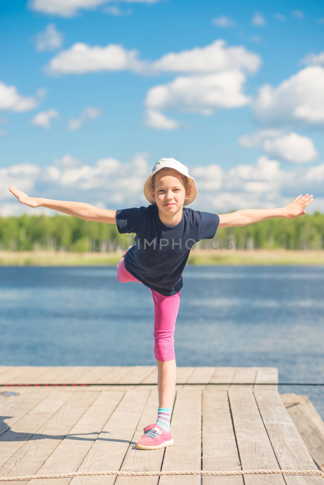 flexible girl on the pier practicing near the water