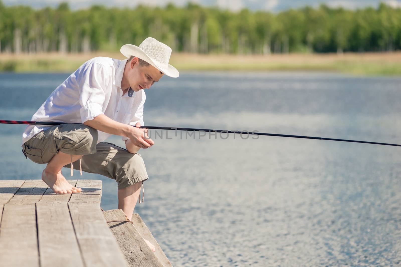 A fisherman in a hat on a wooden pier is fishing on a sunny summer day