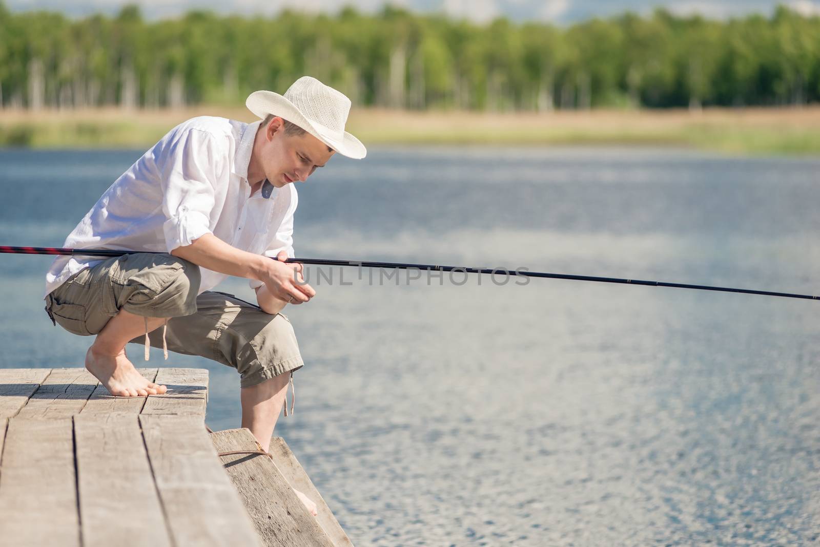 A fisherman in a hat on a wooden pier is fishing on a sunny summ by kosmsos111