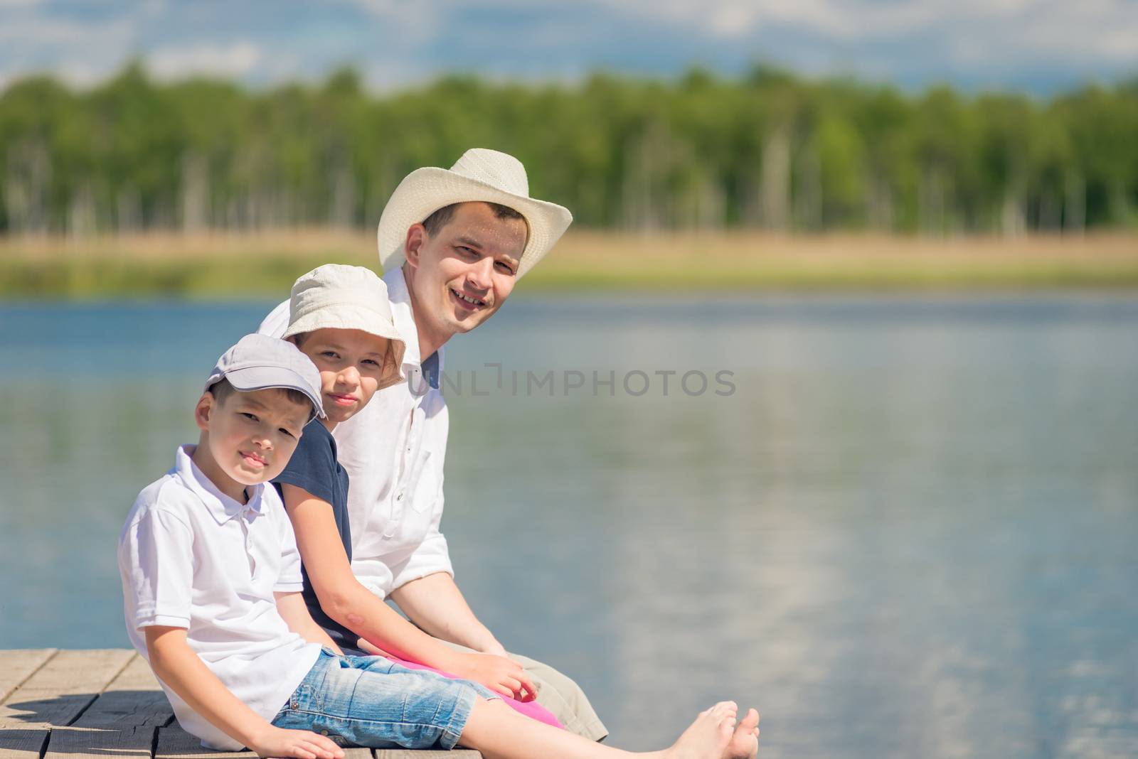portrait of father and children sitting on a wooden pier near the lake