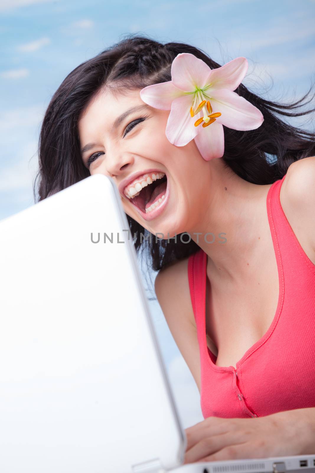 Beautiful laughing girl with lilium in her hair behind laptop